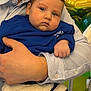 Liam is registered to the contest to win money with this photo: baby, child, person, adult, hand, blue_sweater, striped_shirt, balloons, celebration, indoor, portrait, face, caucasian, holding, closeup, cute, infant, sitting, expressionless, young