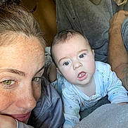 Hudson is registered to the contest to win money with this photo: baby, woman, freckles, blanket, indoor, face, closeup, expression, curious, child, person, skin, hair, eyes, portrait, casual, laying, clothing, toddler, relaxed