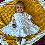 baby, blanket, child, cute, hands, happy, head, indoors, infant, lying_down, person, playful, portrait, skin, smiling, socks, textured_blanket, tongue_out, white_dress, yellow_blanket