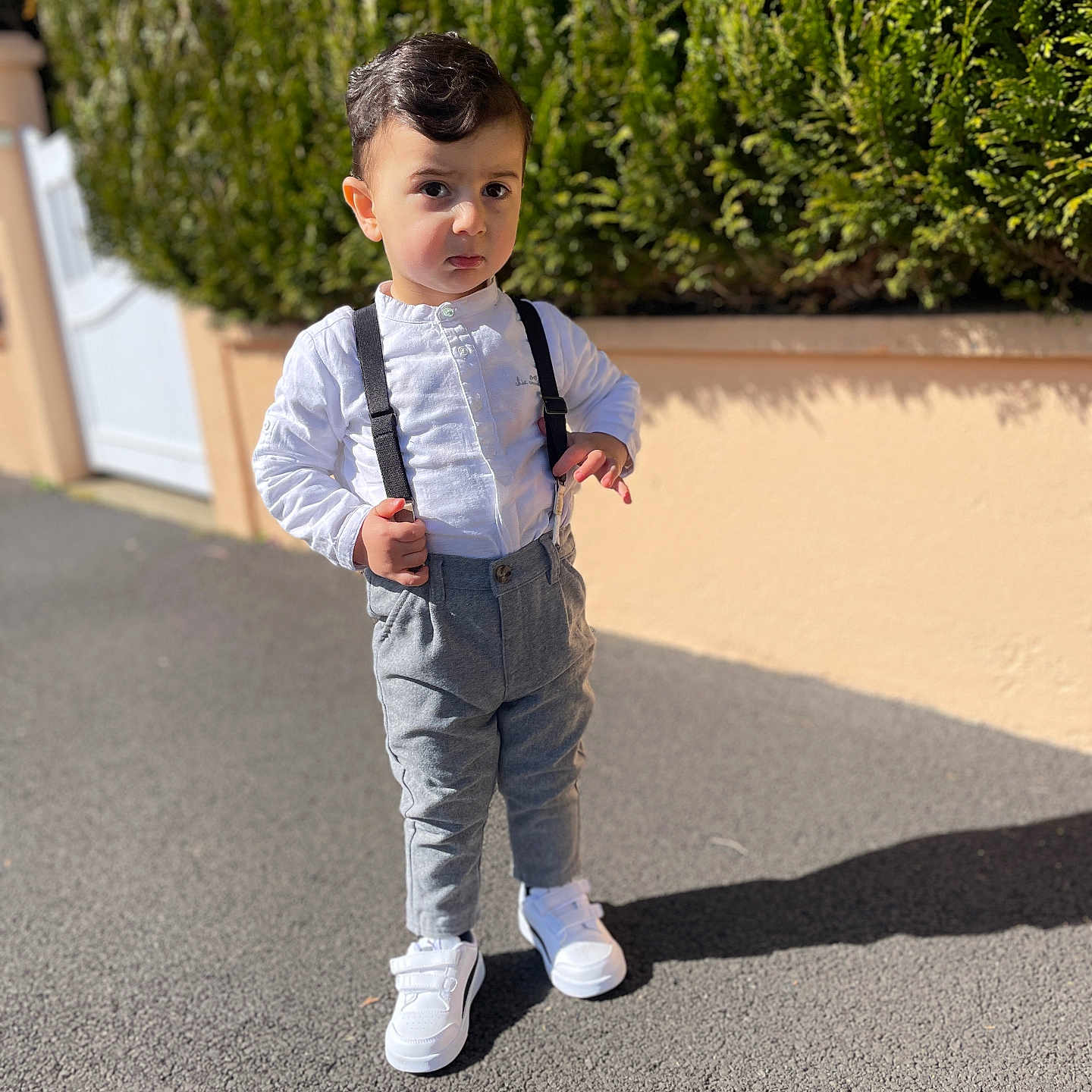 Mika a rejoint le concours — aidez-le/la à gagner de superbes lots ! boy, bushes, casual, child, daylight, expression, fashion, greenery, grey_pants, outdoor, pavement, shadow, short_hair, standing, sunlight, suspenders, toddler, wall, white_shirt, white_shoes