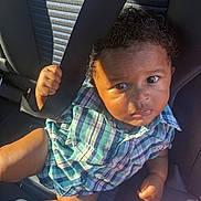 Armani is registered to the contest to win money with this photo: baby, car_interior, car_seat, casual, child, clothing, curly_hair, cute, expression, hand, infant, leg, plaid_shirt, portrait, seat, seatbelt, sitting, socks, sunlight, young_child