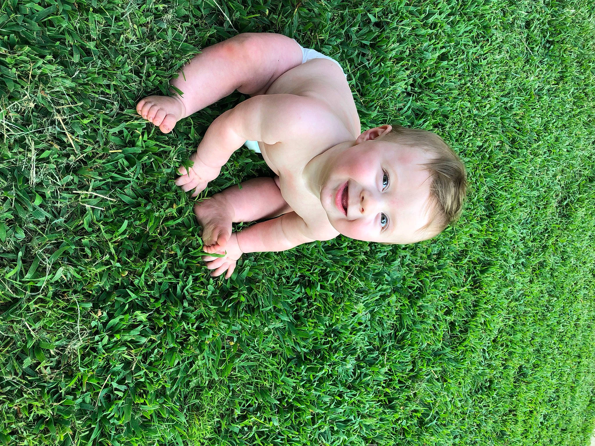 Dean is registered to the contest to win money with this photo: baby, flash_photography, foot, gesture, grass, grassland, groundcover, happy, human_leg, joy, lawn, leisure, meadow, people_in_nature, person, plant, prairie, sitting, thumb, toddler