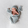 baby, infant, newborn, knitted, blanket, mittens, hat, wrapped, lying_down, white_background, soft_texture, cute, small_hands, portrait, cozy, sleepwear, warm, resting, face, expression