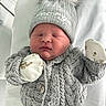 George is registered to the contest to win money with this photo: newborn, baby, sleeping, hat, knitted_sweater, gray, mittens, blanket, indoor, close_up, infant, cute, cozy, resting, hospital, clothing, portrait, child, peaceful, soft