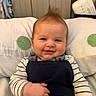George is registered to the contest to win money with this photo: baby, child, smile, face, hair, striped_clothing, pillow, indoor, cute, portrait, infant, hand, sitting, couch, happy, young_child, clothing, person, head, room