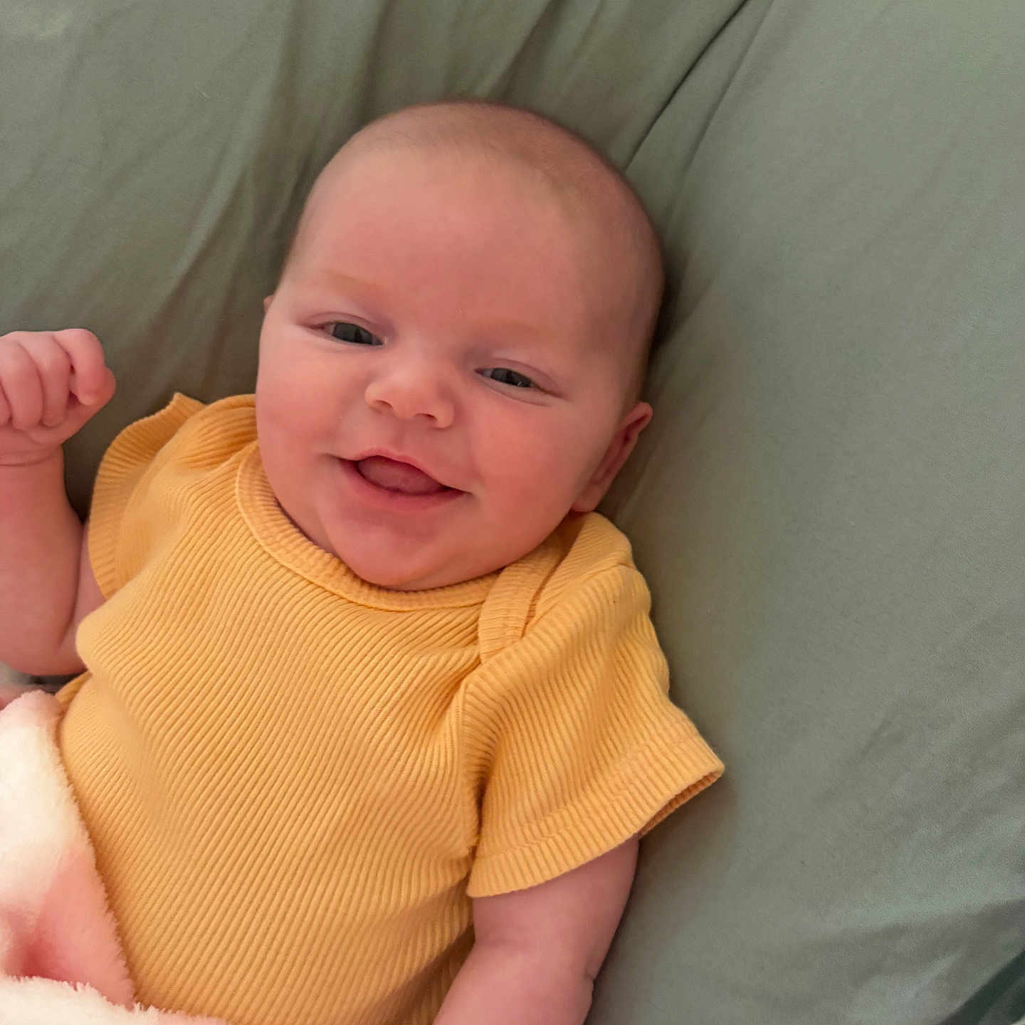 Skyla is registered to the contest to win money with this photo: baby, smiling, yellow_clothing, blanket, infant, lying_down, happy, cute, pink_blanket, green_background, face, skin, head, arm, child, portrait, indoors, soft_texture, cozy, person