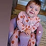 baby, blue_eyes, brown_hair, carpet, child, decorative_text, face, happy, hardwood_floor, home, indoor, infant, infant_seat, photograph, pink_outfit, polka_dots, portrait, radiator, seated, smiling