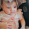 baby, child, infant, portrait, sitting, car_seat, safety_label, bow, headband, dress, peach_clothing, white_blanket, blue_eyes, open_eyes, face, indoors, vehicle, closeup, adorable, photography