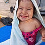toddler, smiling, towel, pink_swimsuit, child, outdoor, happy, sitting, face, baby, blue_mat, footwear, wheel, sunlight, playful, clothing, skin, portrait, young_child, daylight