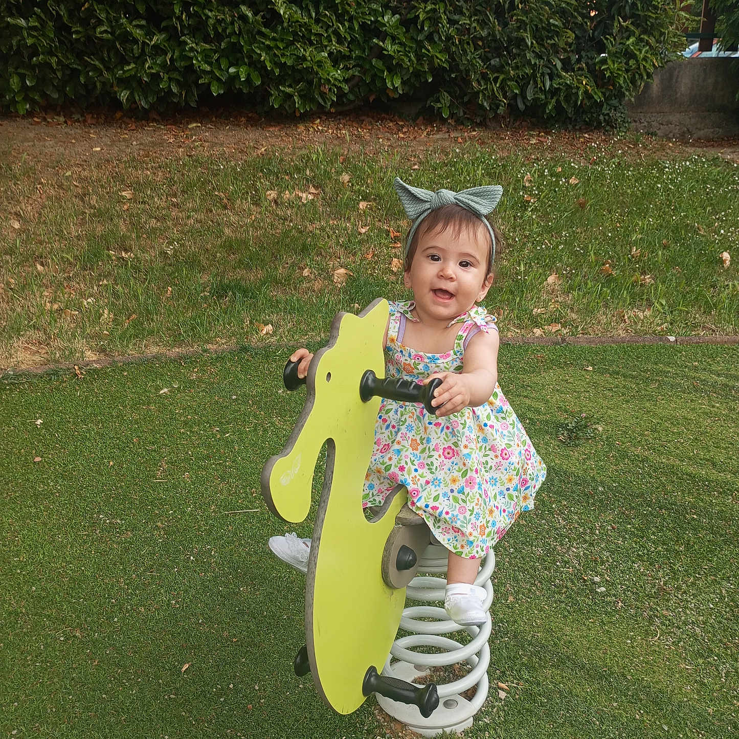 Anna Isabella a rejoint le concours — aidez-le/la à gagner de superbes lots ! bow, bushes, child, daylight, dress, floral_dress, grass, green, happy, headband, nature, outdoor, play, playground, smiling, spring, spring_ride, toddler, toy, white_shoes