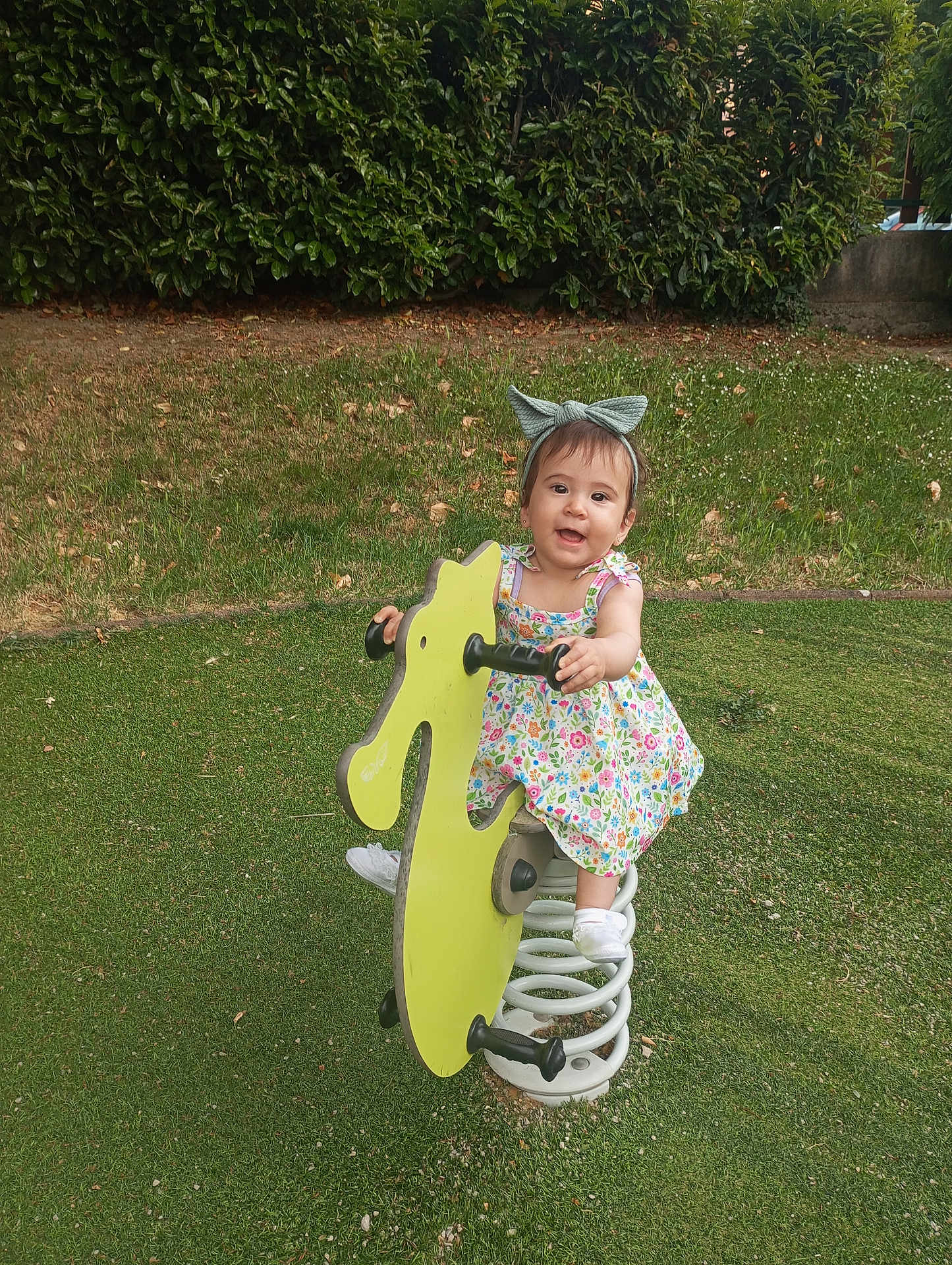 Anna Isabella a rejoint le concours — aidez-le/la à gagner de superbes lots ! child, toddler, playground, spring_ride, green, grass, outdoor, headband, bow, dress, floral_dress, white_shoes, happy, smiling, toy, spring, nature, bushes, daylight, play