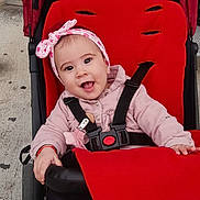 Anna Isabella a rejoint le concours — aidez-le/la à gagner de superbes lots ! baby, child, stroller, red, black, headband, pink, smiling, happy, infant, outdoor, seatbelt, jacket, cute, person, portrait, baby_girl, clothing, sitting, joyful
