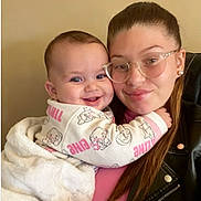 Victoire participe au concours pour gagner de l'argent avec cette photo : baby, child, woman, glasses, smile, hug, blanket, leather_jacket, face, person, indoor, portrait, happy, cozy, clothing, head, affection, cuddle, warm, young