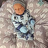 baby, infant, child, portrait, lying_down, onesie, hat, mittens, owl_pattern, elephant_pattern, cushion, pacifier, indoor, home, seated, sleepy, serious_expression, blue_clothing, soft_furnishings, closeup