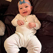 Everly is registered to the contest to win money with this photo: baby, infant, smile, headband, bow, onesie, white_clothing, socks, pillow, bedding, couch, portrait, closeup, happy, chubby_cheeks, hands, lying_down, indoor, cozy, skin