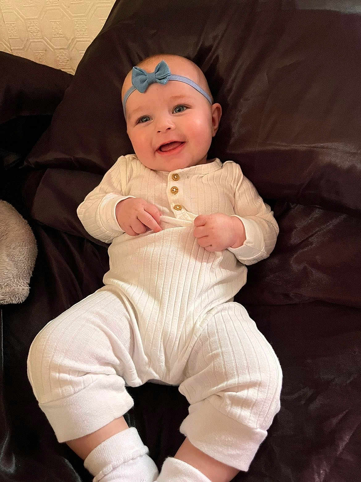 Everly is registered to the contest to win money with this photo: baby, infant, smile, headband, bow, onesie, white_clothing, socks, pillow, bedding, couch, portrait, closeup, happy, chubby_cheeks, hands, lying_down, indoor, cozy, skin