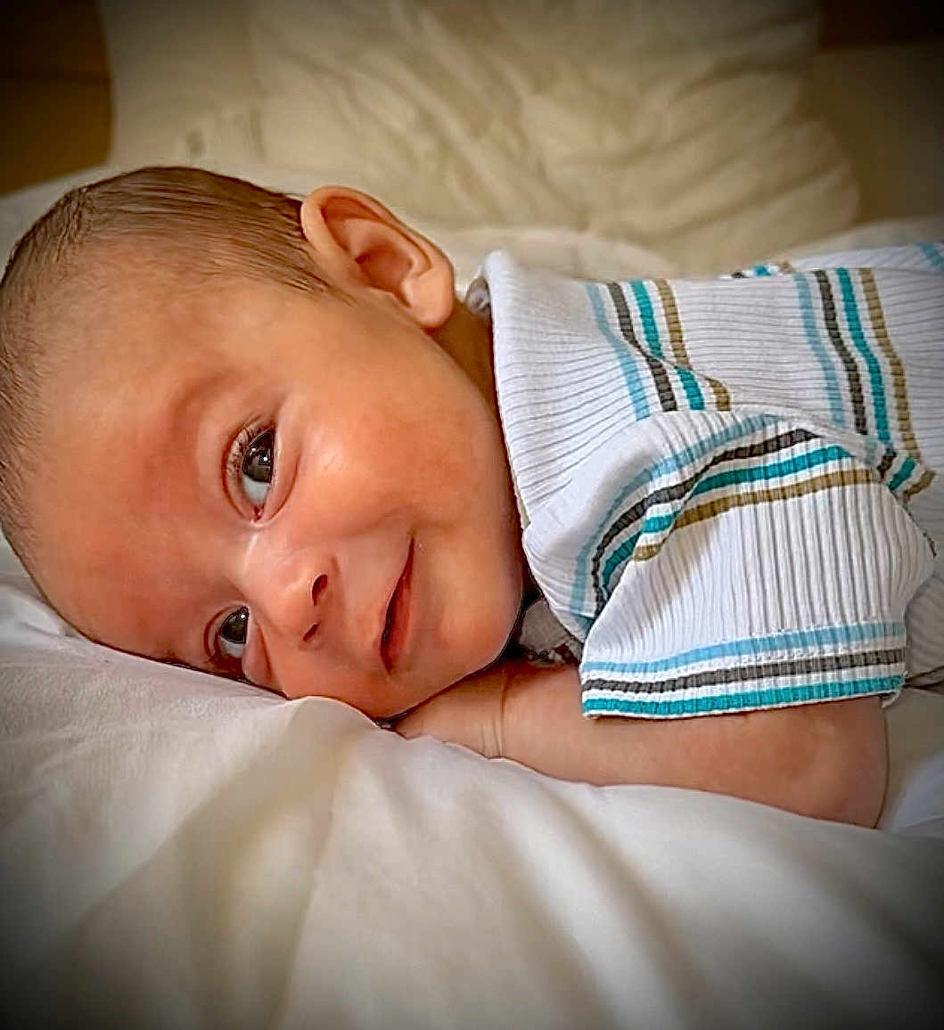 Lyandro Martinez a rejoint le concours — aidez-le/la à gagner de superbes lots ! baby, infant, child, face, portrait, smile, clothing, striped_shirt, lying_down, soft_surface, cute, young, skin, head, eyes, ear, person, indoors, closeup, resting