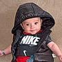 baby, infant, hood, black_vest, red_pants, pacifier, couch, smile, cute, child, portrait, clothing, sitting, indoor, face, person, young, happy, casual, relaxed