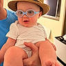 Jonah joined the competition — help win amazing prizes! baby, child, glasses, hat, hand, indoor, person, white_clothing, skin, face, foot, adult, holding, curious, blue, straw_hat, eyewear, smile, closeup, living_room