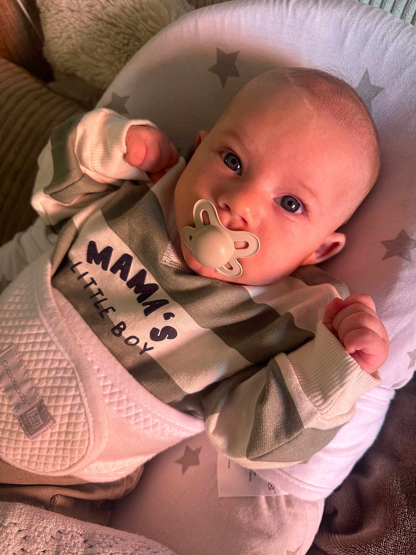 Louis participe au concours pour gagner de l'argent avec cette photo : baby, infant, pacifier, clothing, striped_shirt, text_on_clothing, face, eyes, fist, cushion, star_pattern, blanket, cozy, indoor, cute, newborn, lying_down, child, person, soft_lighting
