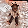Layla is registered to the contest to win money with this photo: baby, child, infant, bed, bedroom, pillow, blanket, hair_bow, person, smiling, sitting, cute, indoors, furniture, nightstand, clothing, skin, foot, hand, happy