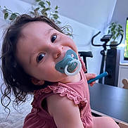 Giovanna a rejoint le concours — aidez-le/la à gagner de superbes lots ! baby, child, curly_hair, cute, exercise_equipment, face, furniture, happy, home, indoor, pacifier, person, pink_dress, plant, playful, portrait, sitting, smile, table, toddler