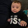 Mathis a rejoint le concours — aidez-le/la à gagner de superbes lots ! adult_partial, baby, black_shirt, child, clothing, couch, cozy, expression, eyes, fabric, face, hair, hand, home, indoor, infant, person, portrait, sitting, text_on_clothing