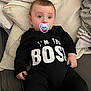 Mathis participe au concours pour gagner de l'argent avec cette photo : baby, black_onesie, blanket, casual, child, couch, cute, home, indoors, infant, looking_away, pacifier, person, pillow, portrait, relaxed, sitting, small_hands, soft_furnishing, text_on_clothing