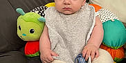 Mathis participe au concours pour gagner de l'argent avec cette photo : baby, bib, bottle, child, clothing, colorful, comfort, cushion, cute, expression, face, foot, hand, home, indoors, infant, pacifier, plush_toy, sitting, sofa