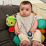 baby, bib, bottle, child, clothing, colorful, comfort, cushion, cute, expression, face, foot, hand, home, indoors, infant, pacifier, plush_toy, sitting, sofa
