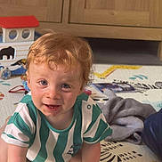 Sebastian joined the competition — help win amazing prizes! toddler, child, baby, curly_hair, crawling, play_mat, toys, blanket, indoor, wooden_cabinet, home, smiling, cute, person, clothing, striped_shirt, floor, happy, face, blue_eyes