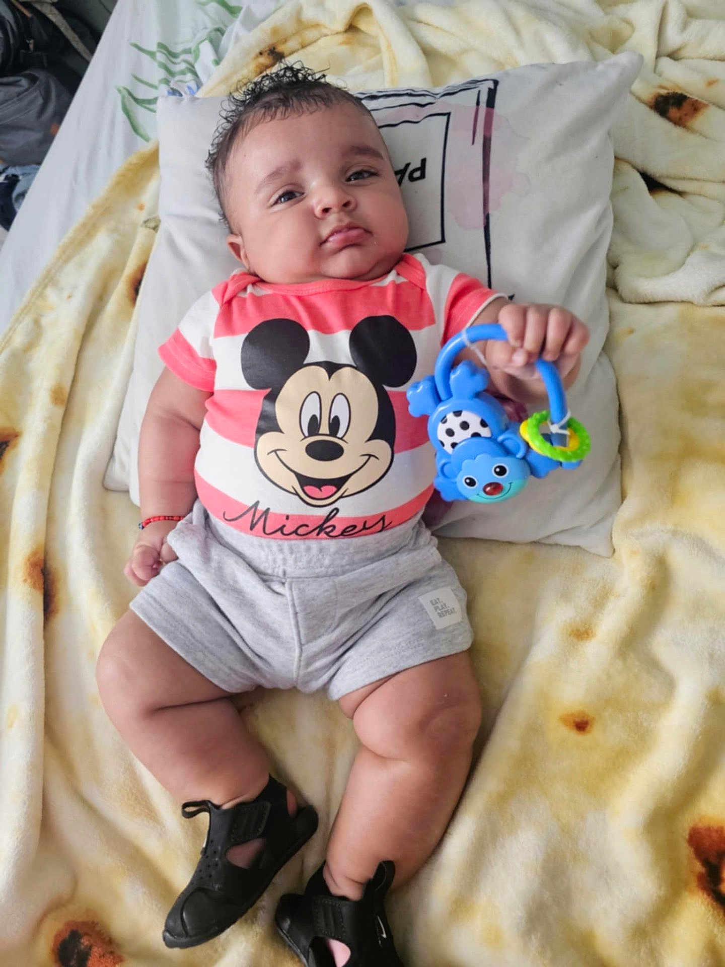 Yassiel Torres joined the competition — help win amazing prizes! baby, black_shoes, blanket, child, colorful, cute, face, footwear, hand, indoors, infant, legs, lying_down, mickey_mouse, pillow, shirt, shorts, smiling, soft_texture, toy