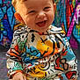 baby, child, smiling, colorful_clothing, graffiti, urban, mural, happy, face, portrait, sitting, hoodie, playful, cute, street_art, vibrant, young_child, casual, background, expression
