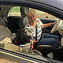 car, casual_clothing, daytime, dog, driver, happiness, human, joy, leisure, older_adult, pet, roadside, seat, seatbelt, smile, sunlight, tongue_out, vehicle_interior, window, woman