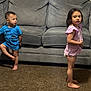 toddler, child, indoor, living_room, couch, carpet, barefoot, blue_shirt, pink_dress, curious, standing, two_children, young, home, casual, short_hair, long_hair, expression, furniture, playful