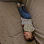 toddler, child, couch, upside_down, clothing, pants, shirt, face, looking, beige, quilted, furniture, indoor, floor, wooden_floor, socks, person, young_child, casual, relaxed