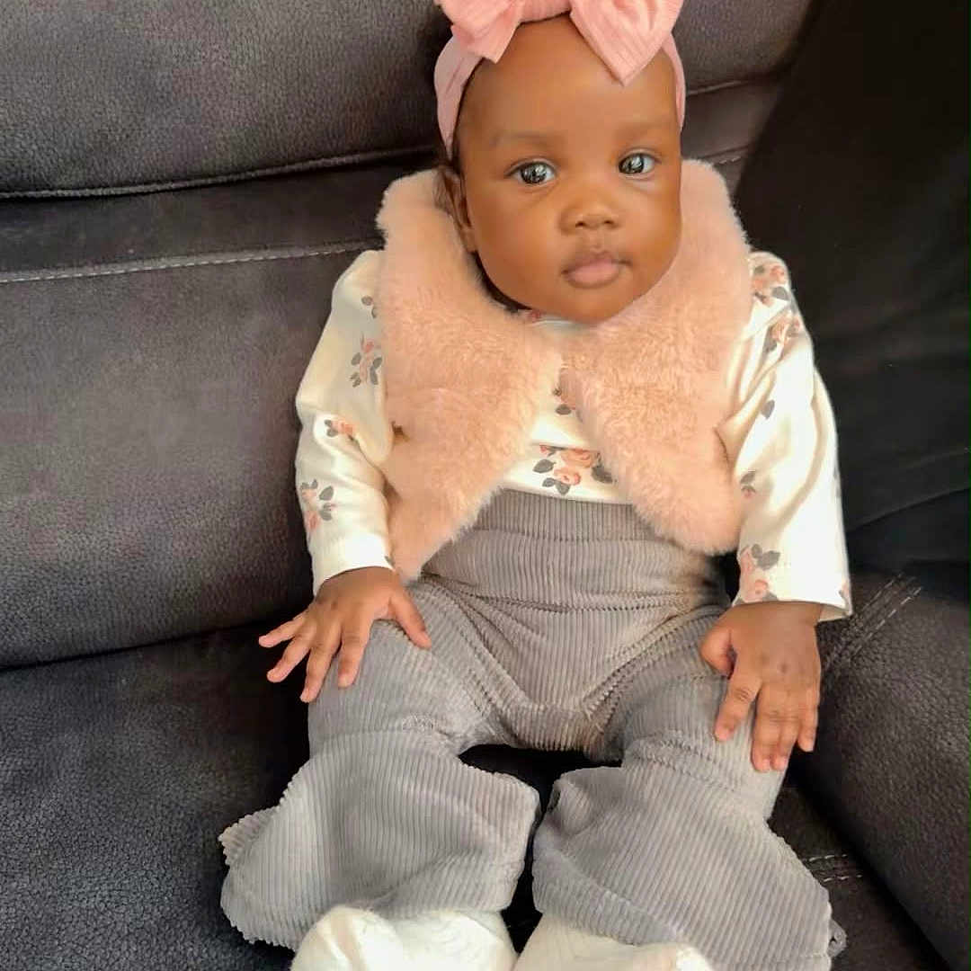 Ayla Makoni is registered to the contest to win money with this photo: baby, child, infant, girl, couch, pink_bow, headband, vest, floral_shirt, corduroy_pants, white_socks, seated, indoor, portrait, cute, hands, face, eyes, clothing, furniture
