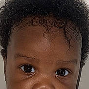 Ayla Makoni joined the competition — help win amazing prizes! baby, child, portrait, face, curly_hair, close_up, skin, eyes, expression, infant, young_child, cute, head, person, indoors, neutral_background, human, looking, baby_skin, calm
