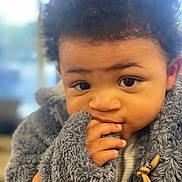 Kairo is registered to the contest to win money with this photo: child, baby, curly_hair, fuzzy_jacket, hand, face, eyes, portrait, cute, indoor, warm_clothing, expression, fingers, young_child, closeup, person, soft_texture, innocent, cozy, curious