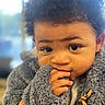 child, baby, curly_hair, fuzzy_jacket, hand, face, eyes, portrait, cute, indoor, warm_clothing, expression, fingers, young_child, closeup, person, soft_texture, innocent, cozy, curious