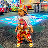 toddler, child, boy, clothing, mickey_mouse, overalls, cap, shoes, indoor, arcade, play_area, carpet, people, family, game_machine, colorful, floor, standing, portrait, entertainment_center