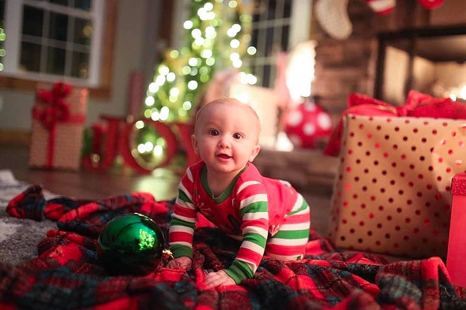 Nash is registered to the contest to win money with this photo: baby, child, christmas, christmas_decoration, christmas_eve, christmas_ornament, christmas_tree, event, holiday, interior_design, person, play, red, sitting, smile, toddler, tree