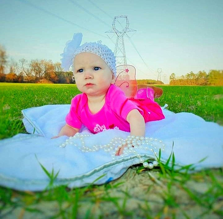 Liberty is registered to the contest to win money with this photo: baby, baby_toddler_clothing, face, facial_expression, flash_photography, fun, grass, grassland, happy, hat, headwear, leisure, mammal, people_in_nature, person, petal, pink, plant, sky, toddler
