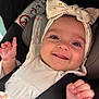 baby, smiling, headband, car_seat, safety_belt, infant, cute, hand, face, clothing, happy, child, portrait, closeup, seat, fabric, cute_expression, person, baby_girl, accessory