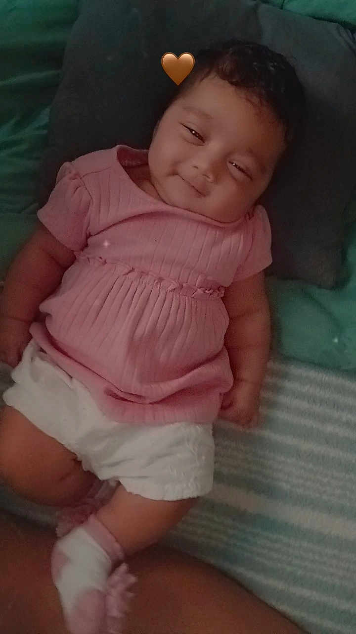 D'Zakaryi joined the competition — help win amazing prizes! baby, infant, pink_clothing, white_shorts, smiling, lying_down, pillow, blanket, heart_emoji, cute, child, indoors, cozy, soft_lighting, portrait, happy, toddler, childhood, resting, casual