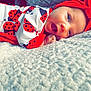 baby, infant, child, smiling, red_headband, ladybug_outfit, blanket, soft_texture, lying_down, cute, happy, face, portrait, closeup, indoors, cozy, bright_colors, skin, hand, expression