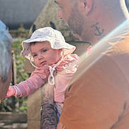Valentina participe au concours pour gagner de l'argent avec cette photo : arm, baby, blurred_background, casual, child, clothing, cute, expression, face, hat, holding, interaction, man, nature, outdoor, person, portrait, skin, sunlight, tattoo