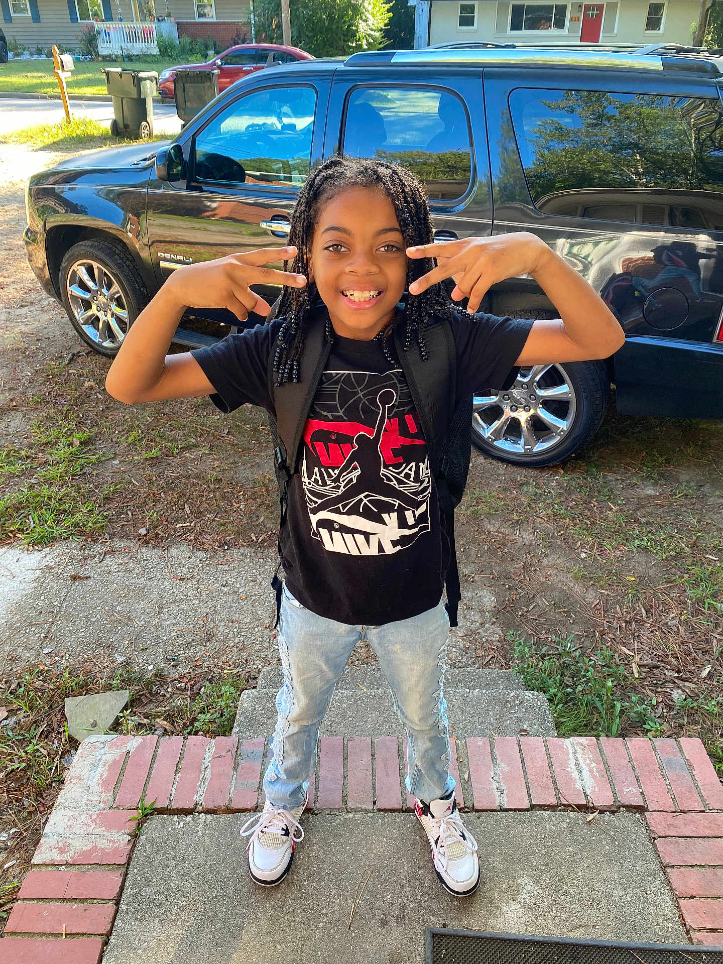Noah joined the competition — help win amazing prizes! child, smiling, posing, braided_hair, black_tshirt, jeans, sneakers, backpack, front_porch, concrete, brick, car, suv, suburban, street, mailbox, trash_bins, daylight, outdoor, happy