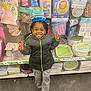 child, birthday_hat, smiling, peace_sign, party_supplies, store_aisle, jackets, sweatpants, crocs, happy, indoor, colorful, celebration, toys, decorations, face, person, retail, shopping, floor