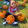 casual_clothing, child, curly_hair, daylight, fall, festival, fun, grass, harvest, nature, orange, outdoor, person, playing, puma_shirt, pumpkin, sitting, sneakers, toddler, young_child